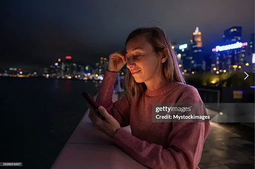 Young woman in pink sweater using phone by waterfront at night media library image media library image woman using phone at night